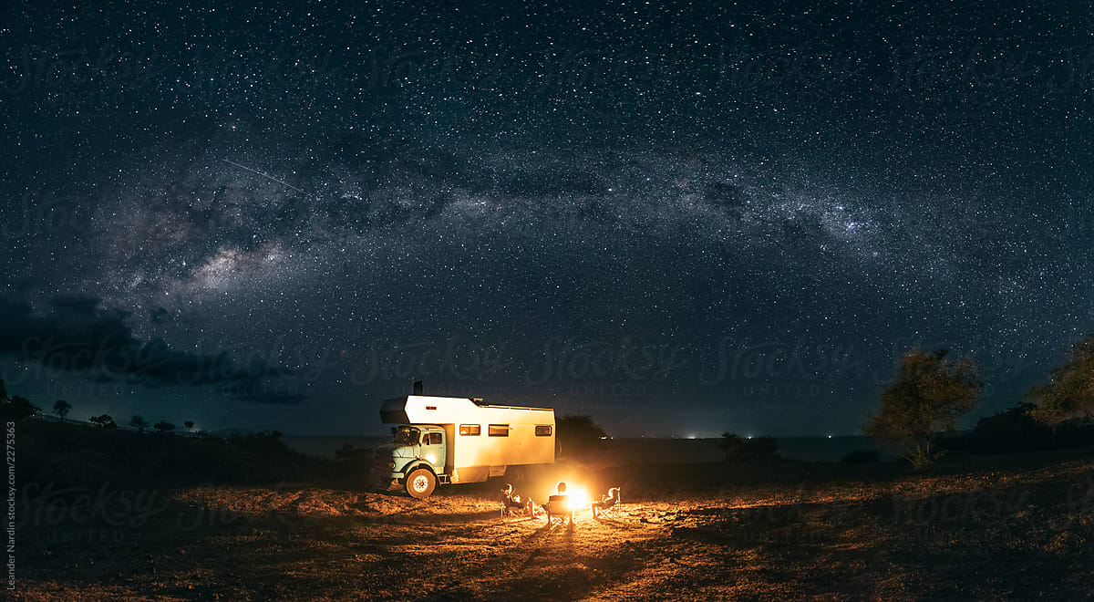 panorama shot of a family sitting at a bonfire under the milky way with a camping truck