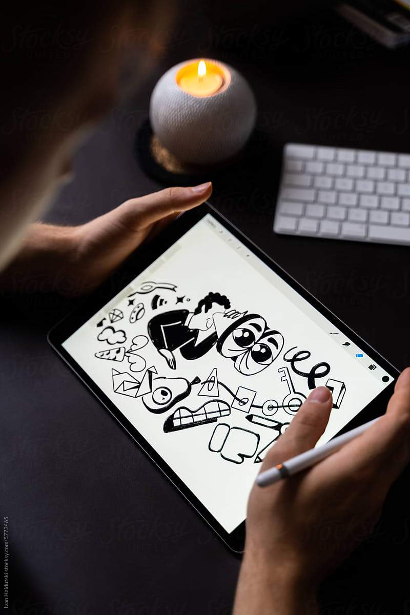 Unrecognized man drawing illustrations on tablet at dark workspace
