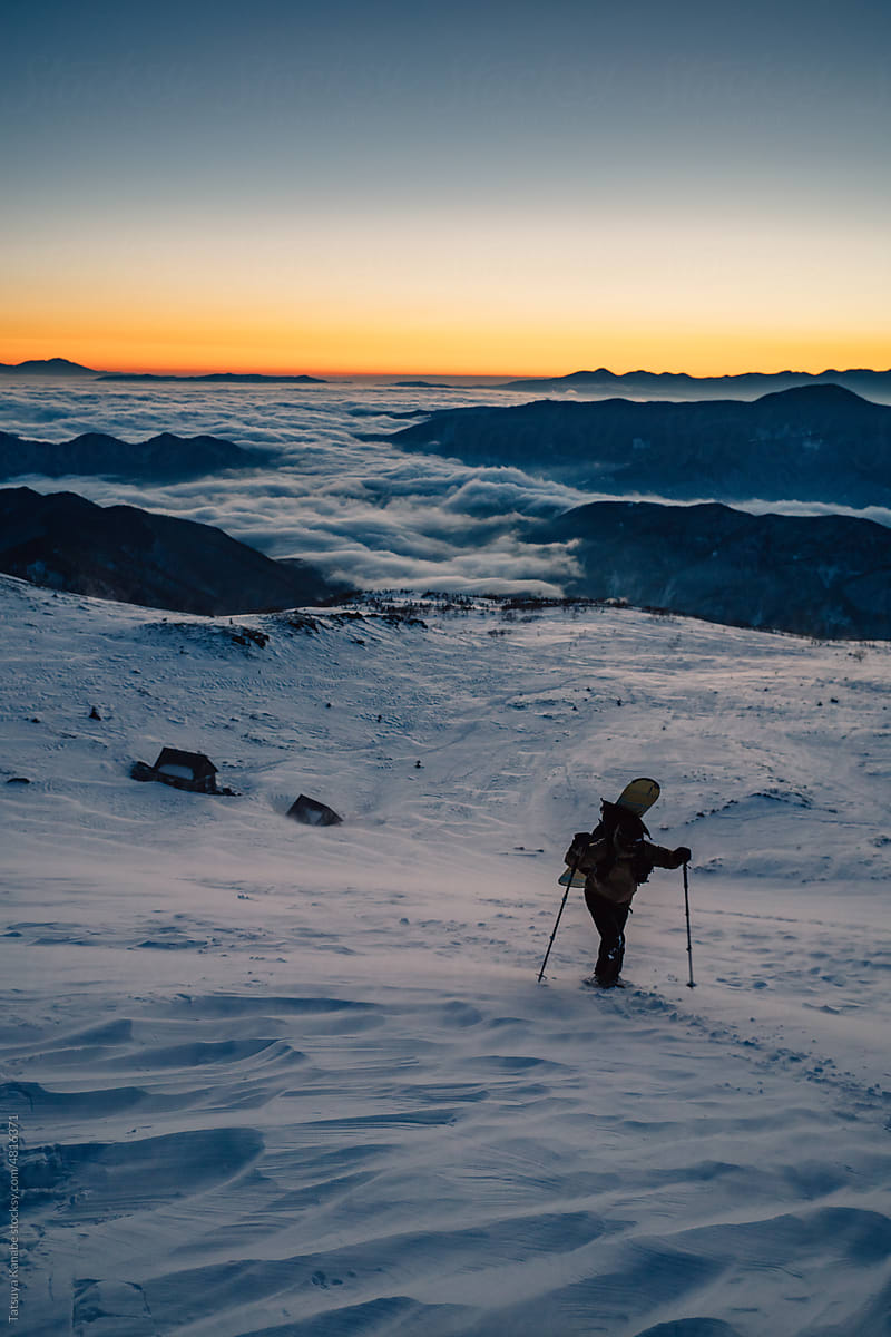 Traveler with trekking poles on snowy mountain slope