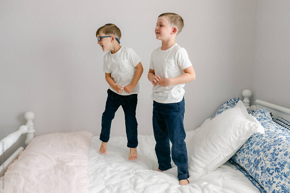 Two boys jump on a white bed