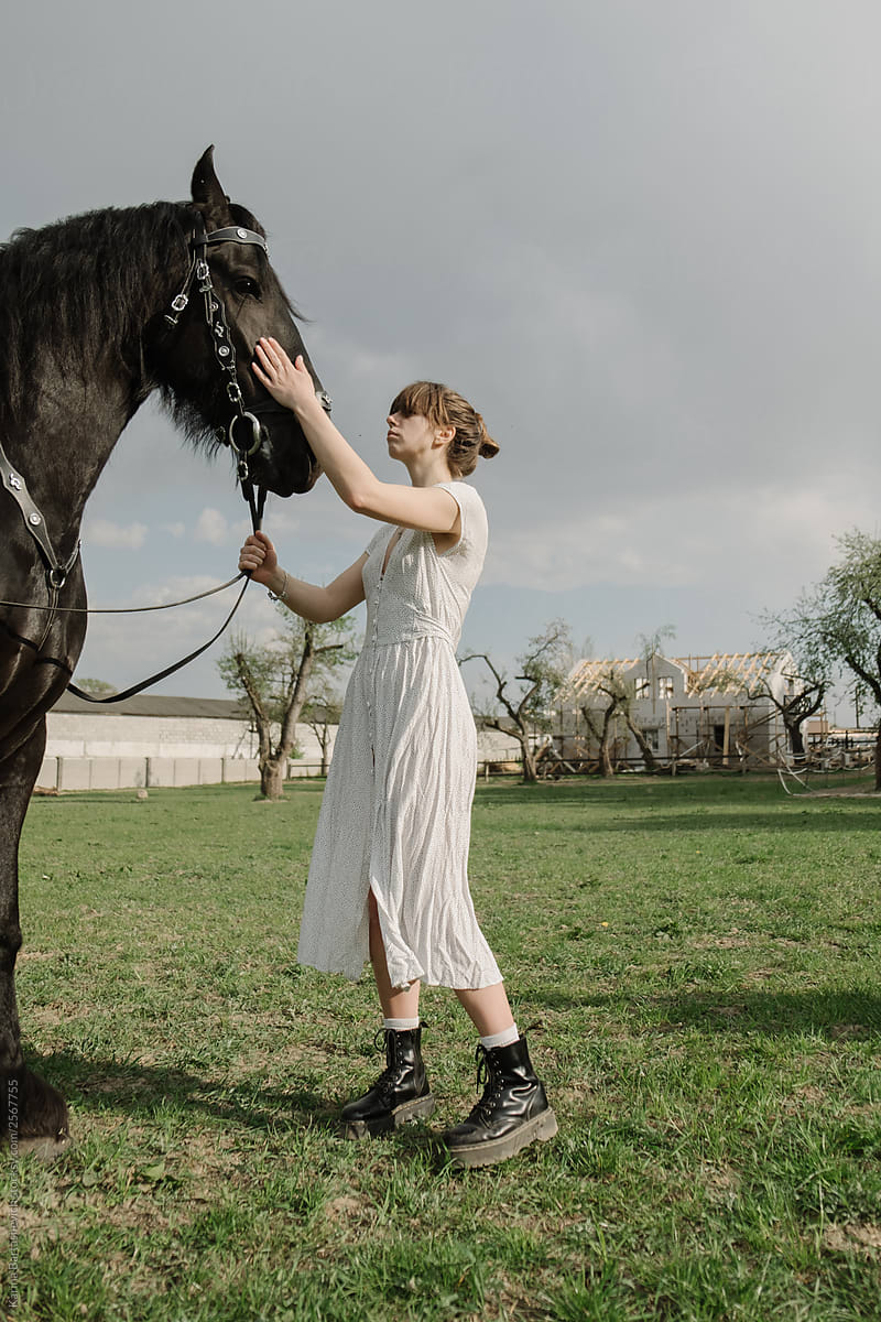 Beautiful and stylish girl in a dress that strokes a horse