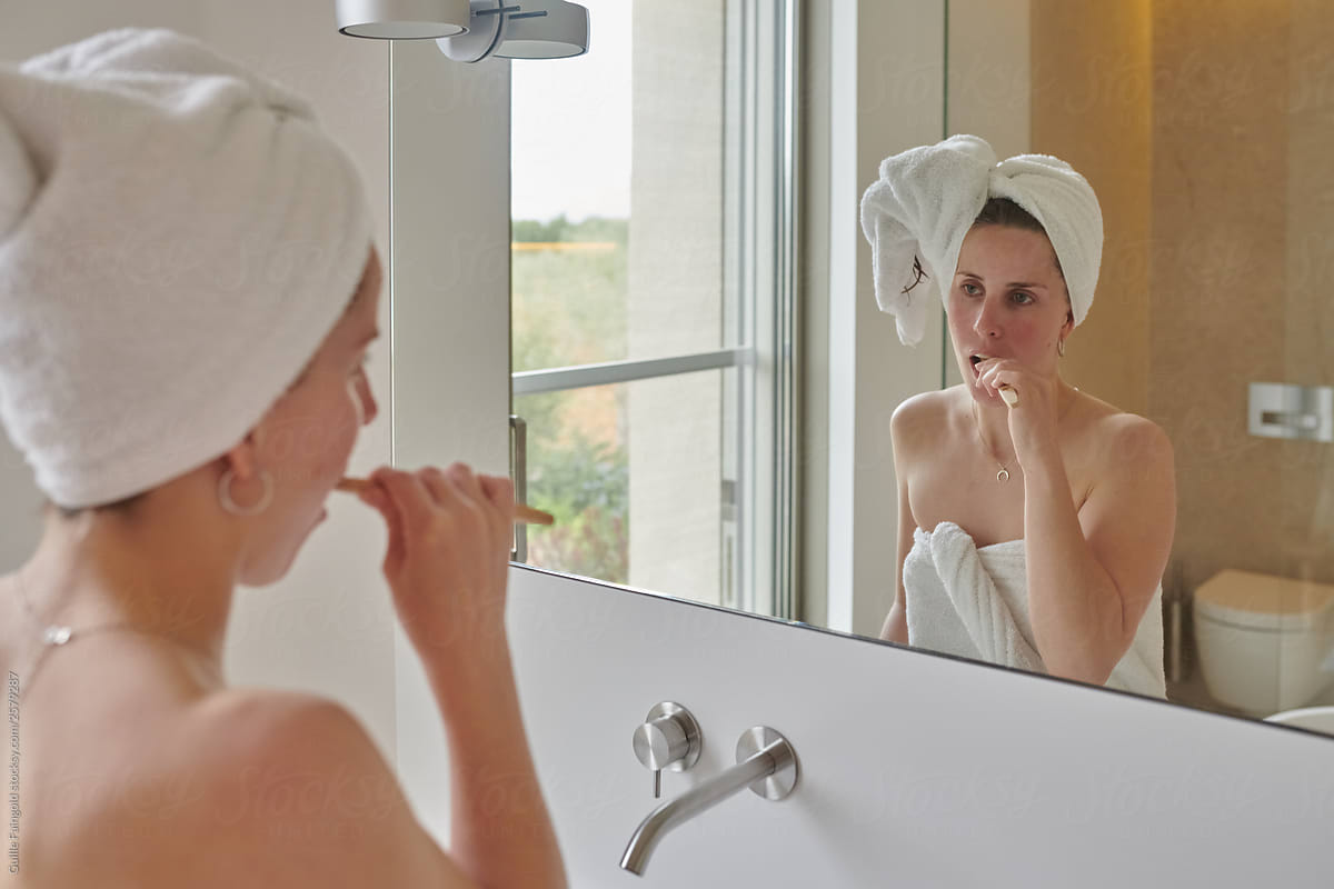 Woman wrapped in towel brushing teeth in bathroom