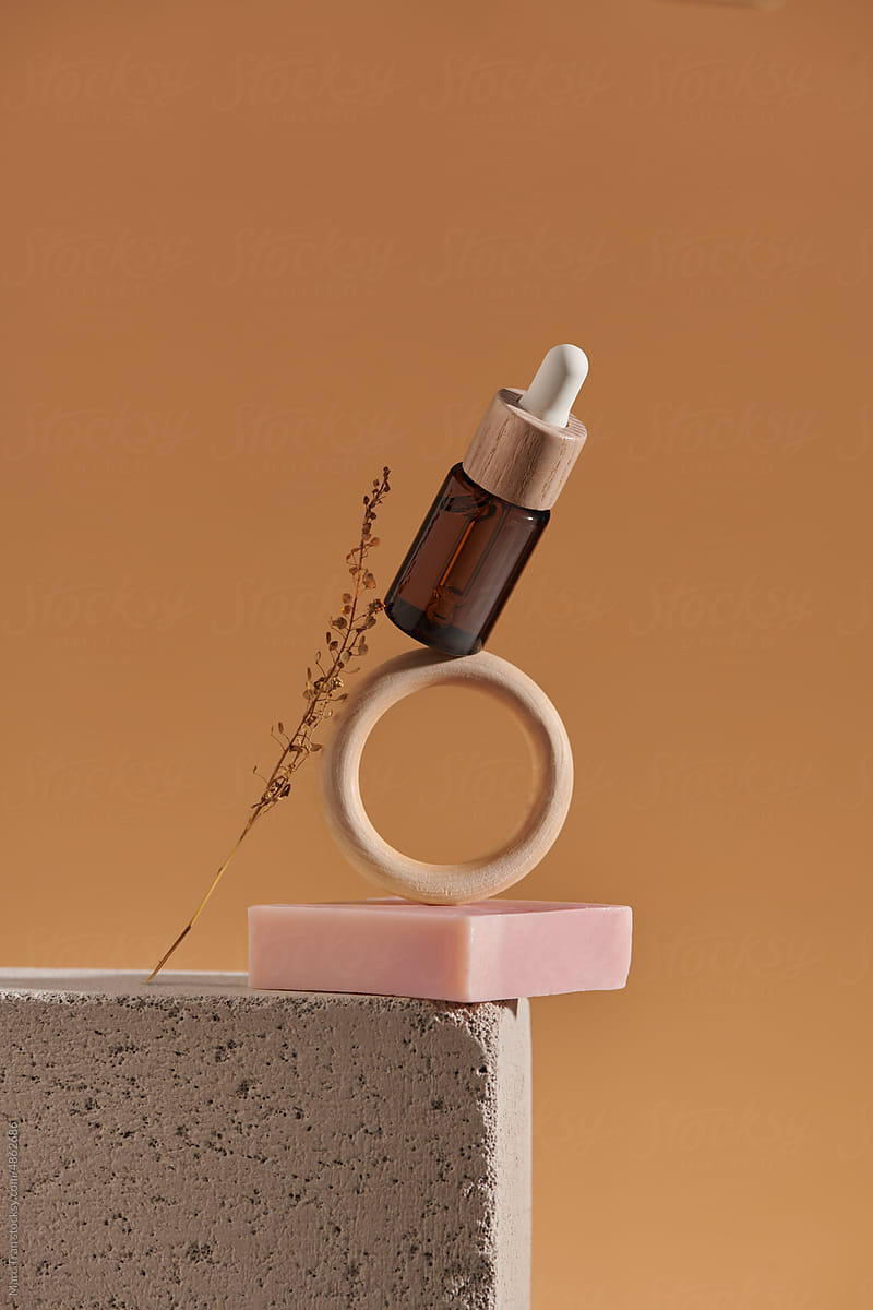 Bottle of essential oil, soap bar stand balancing on brown background