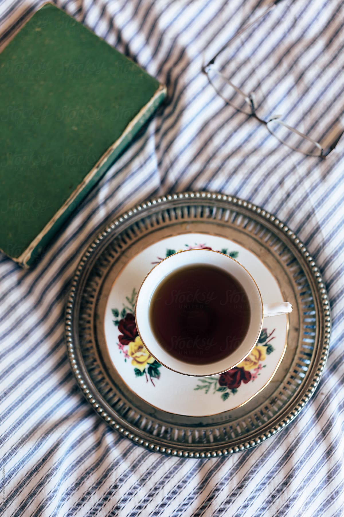 Overhead view of black tea in china cup on vintage tray with closed book and glasses