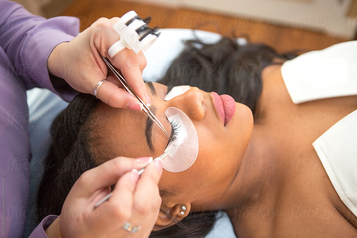 Lash technician gluing a temporary fake lash to a young black woman