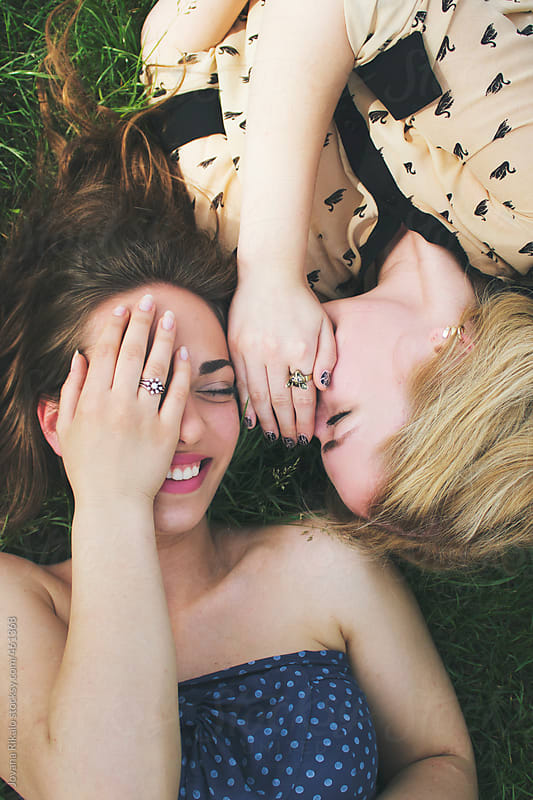 Two female friends are lying on grass and laughing by Jovana Rikalo for Stocksy United
