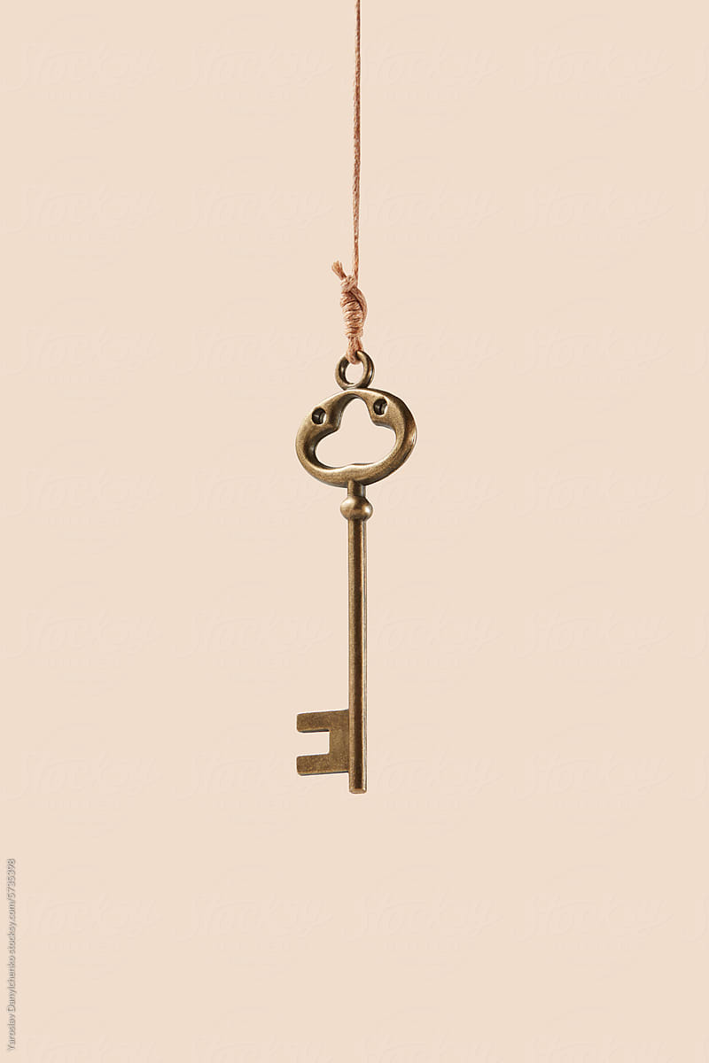 Bronze vintage key hanging on thread over beige background