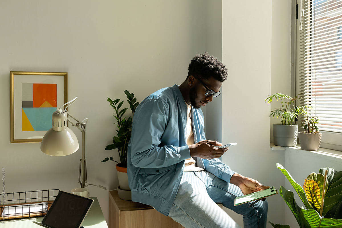 African man browsing on phone at bright workspace