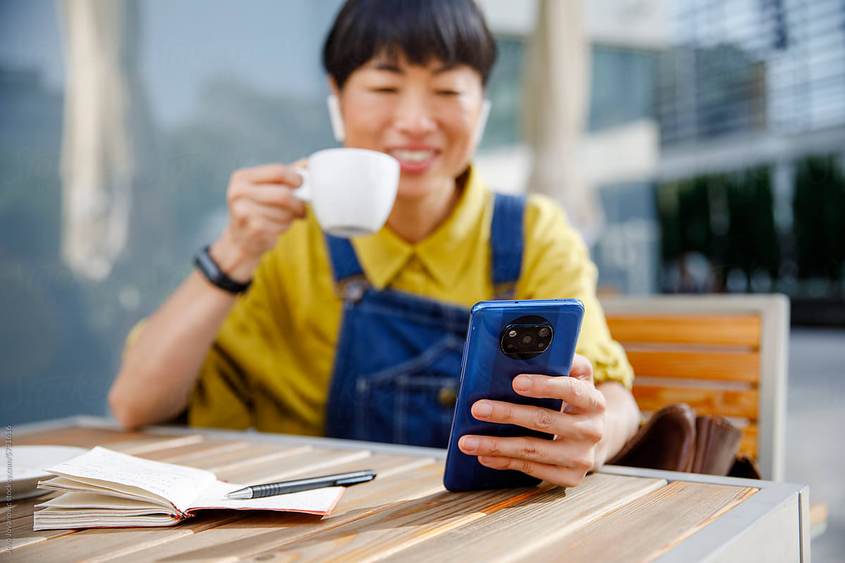 Woman having coffee while discussing through videocall on phone