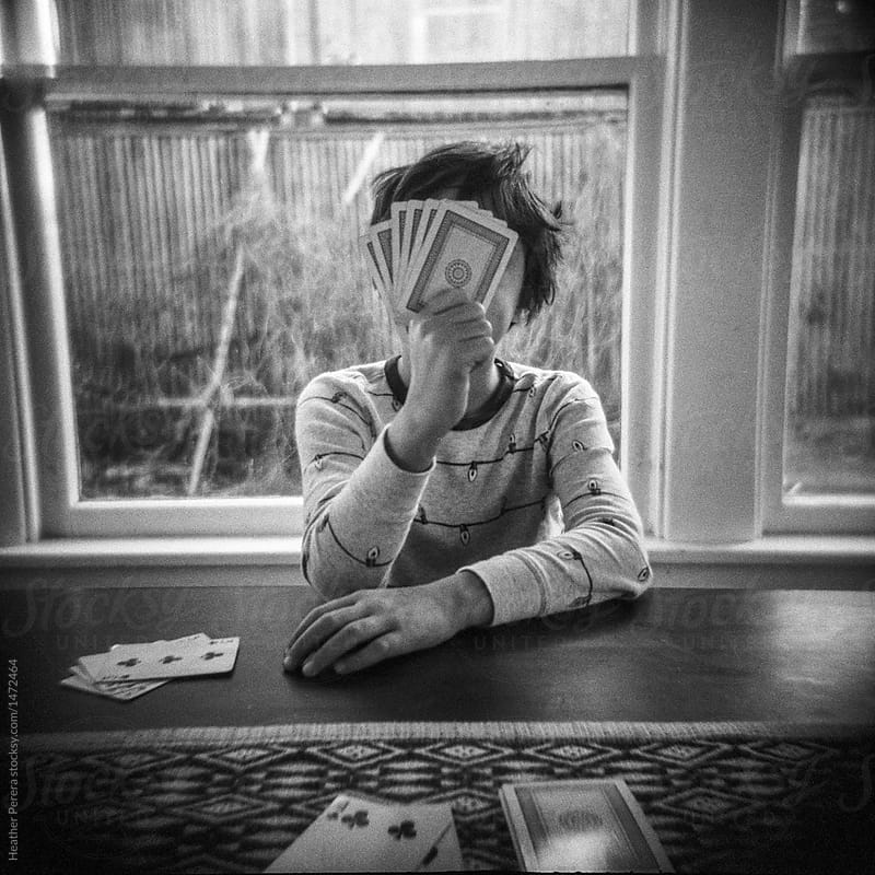 boy hiding face playing cards