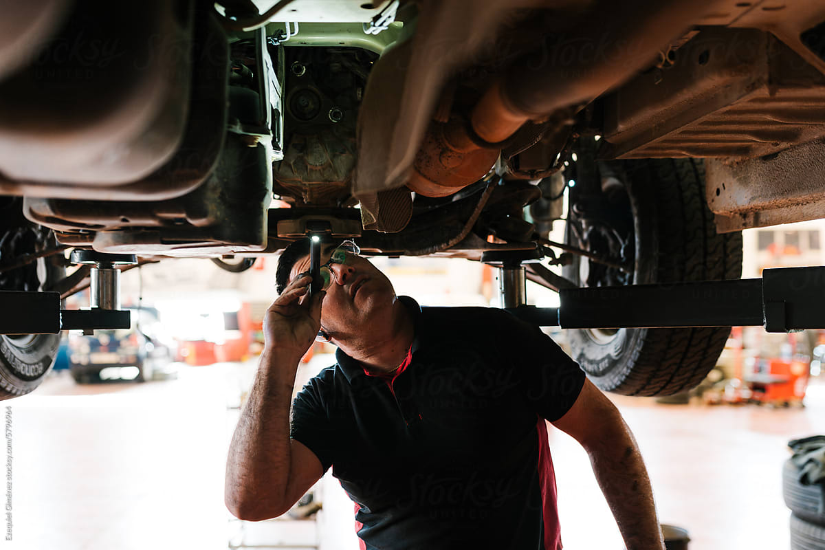 Focused male mechanic examining chassis of suspended car in workshop