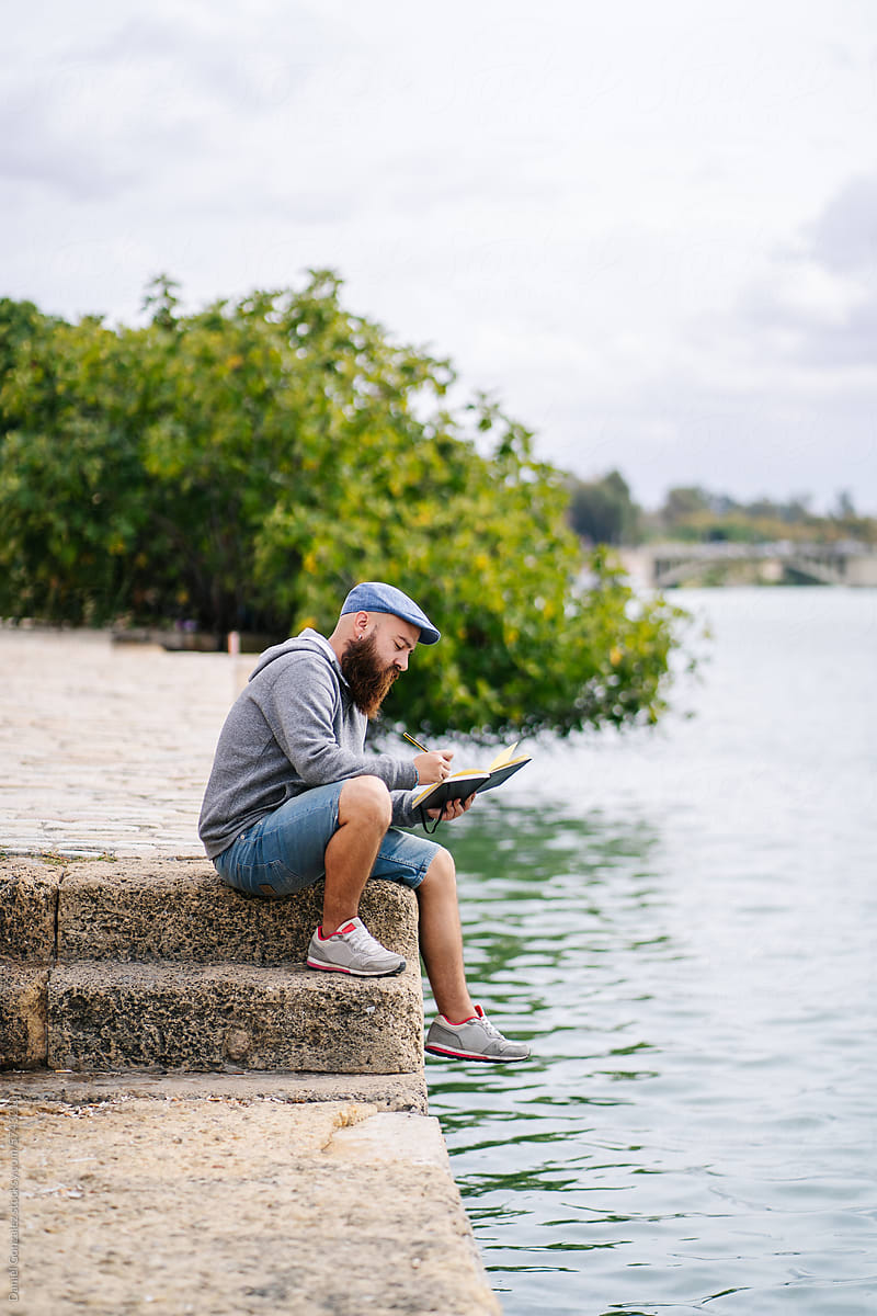 Male sitting on waterfront and checking notebook