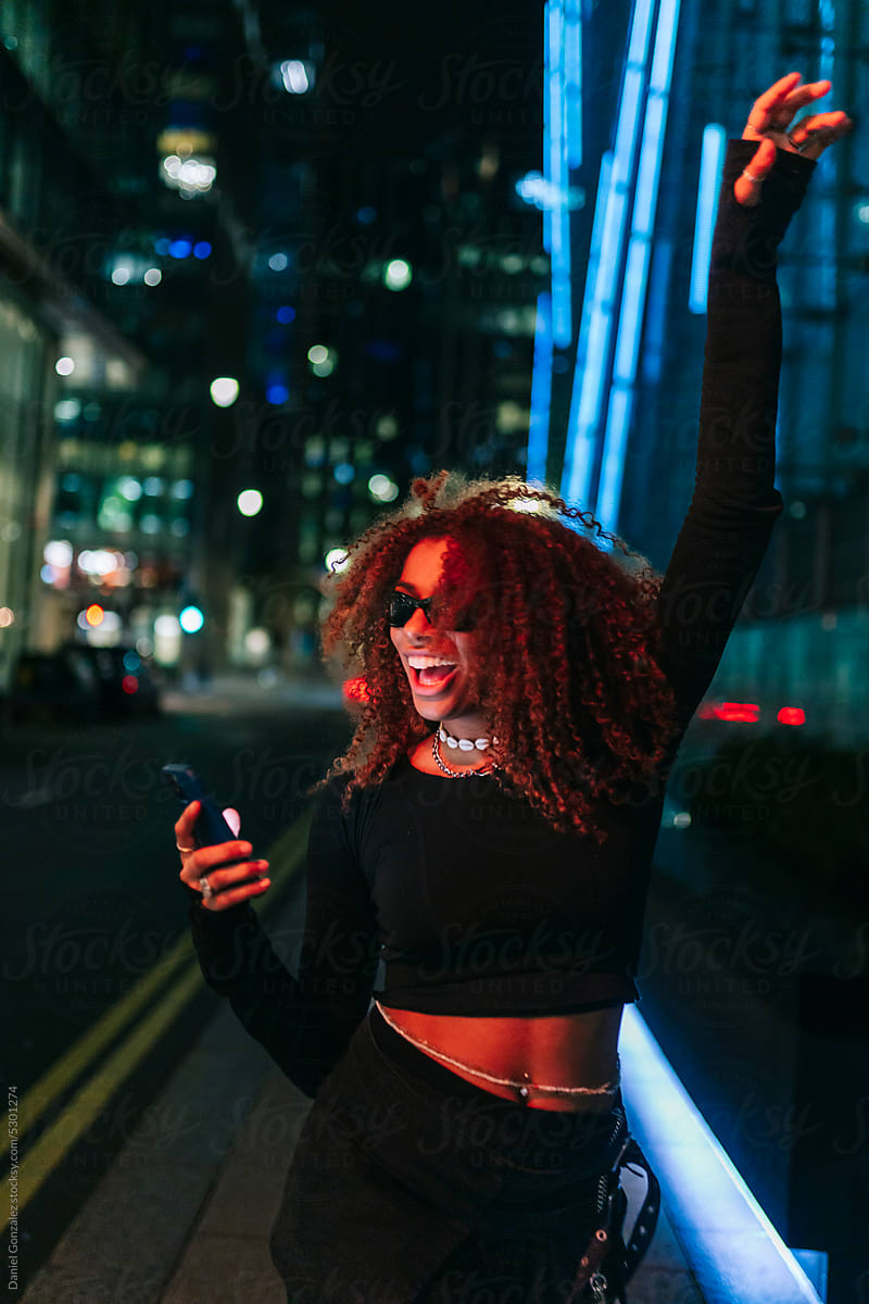 Happy African American lady using phone on night street