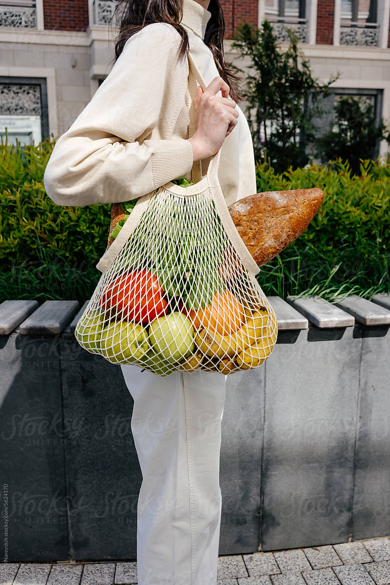 Crop woman with mesh bag of groceries on shoulder