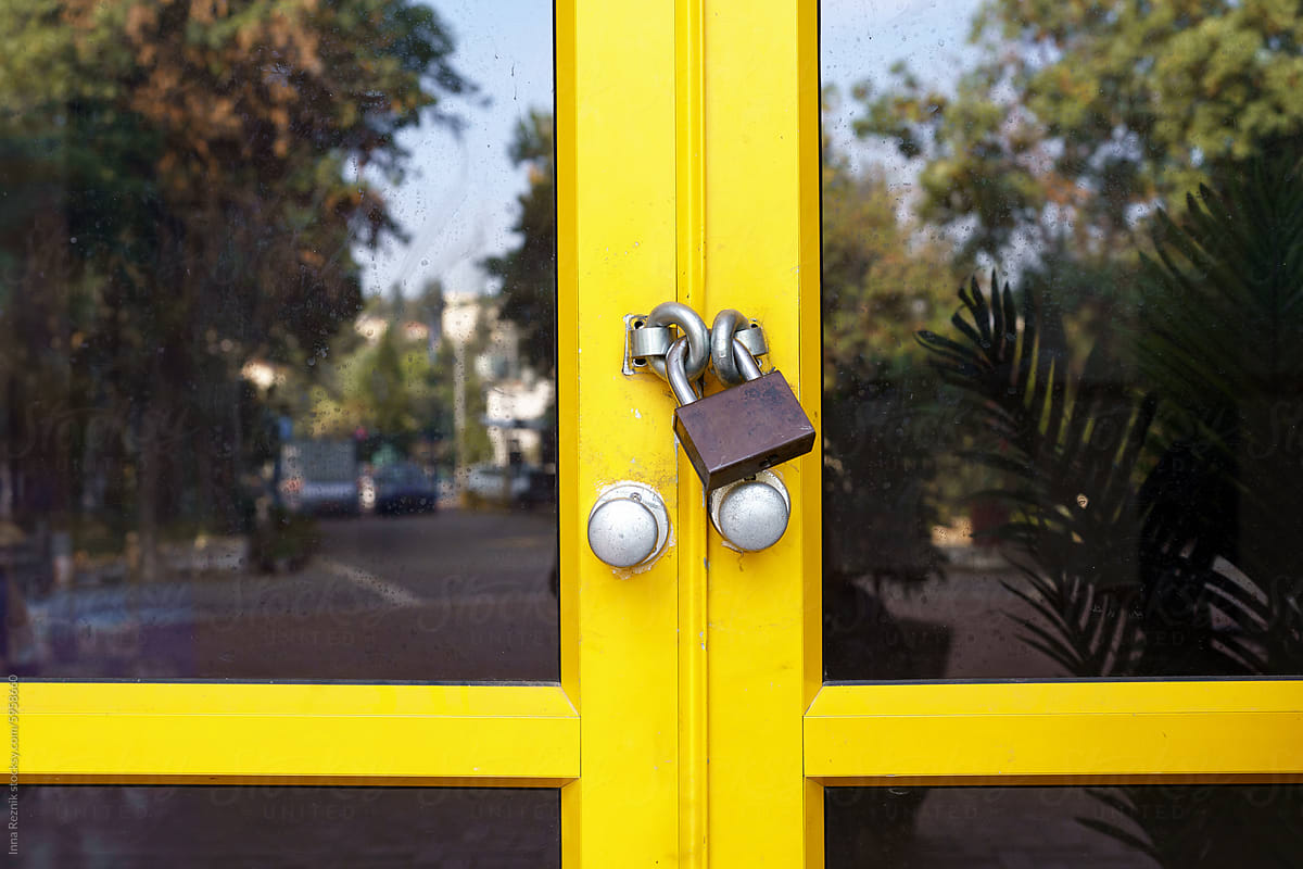 Locked Yellow School Doors Secured With Padlock With Street Reflection