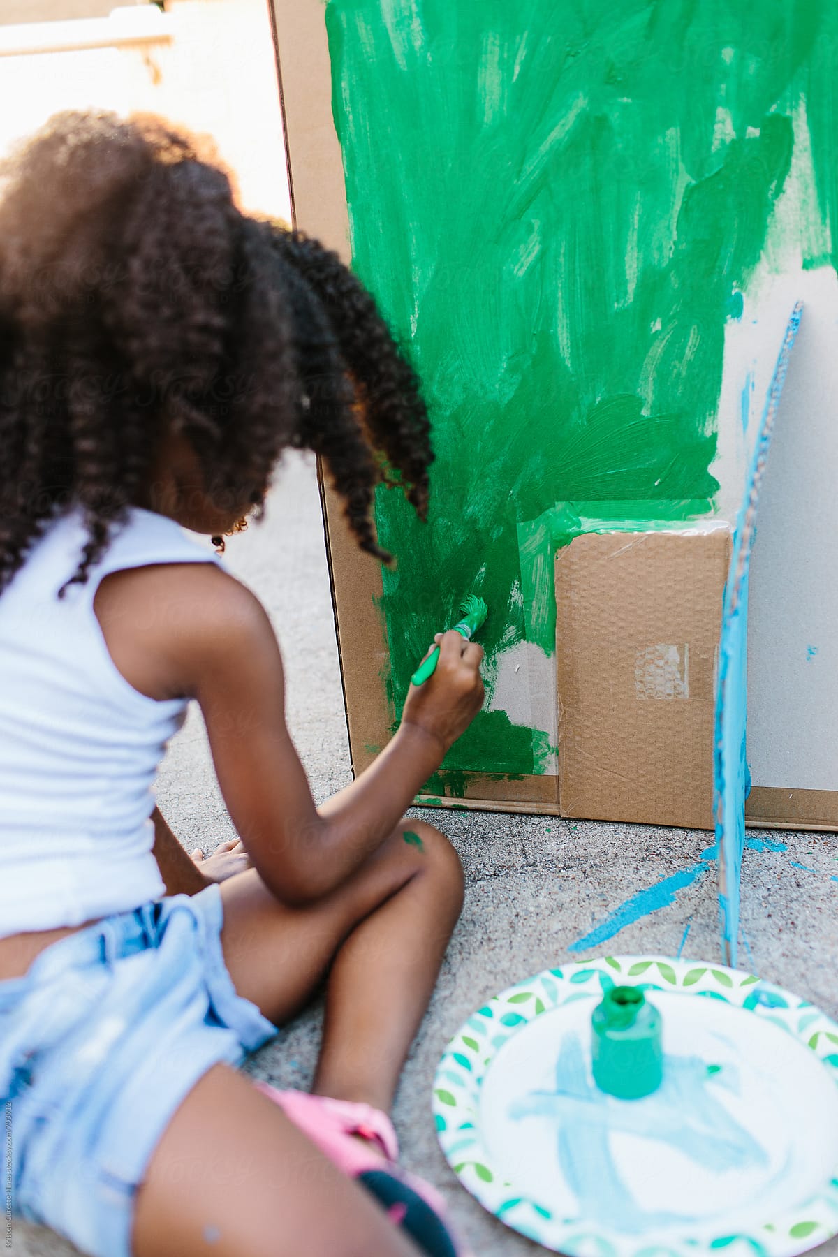A child painting a card board box green