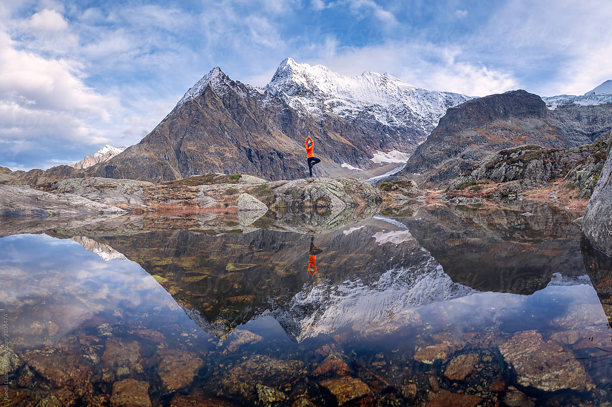 Outdoor girl doing yoga at mirror-like lake in the swiss alps.