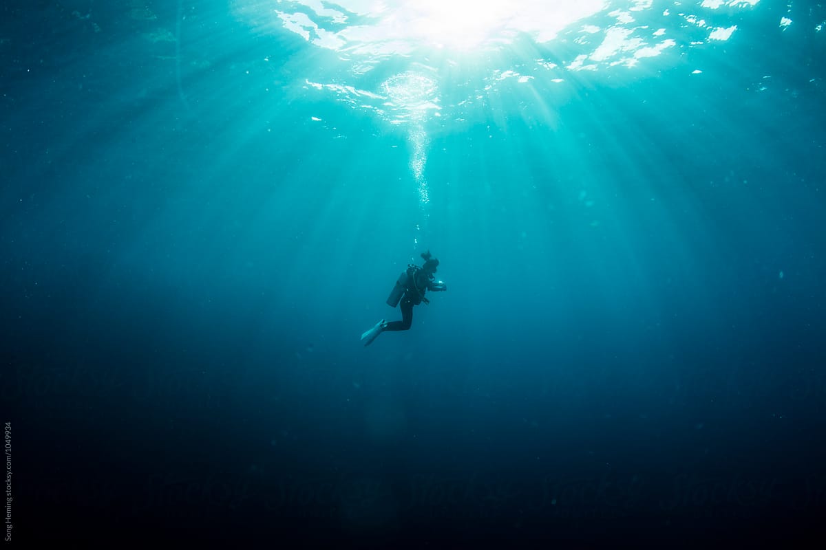 A scuba diver diving under sunlight