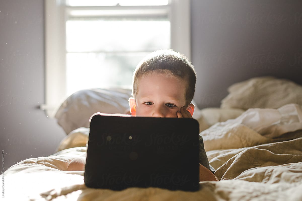 Young boy lying on bed playing with a tablet