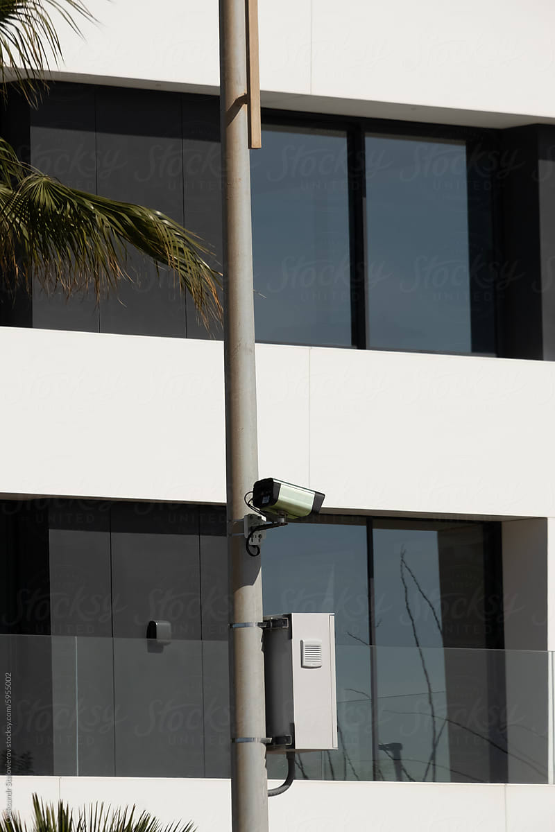 Speed camera on pillar.\
White luxury house with palms on background.