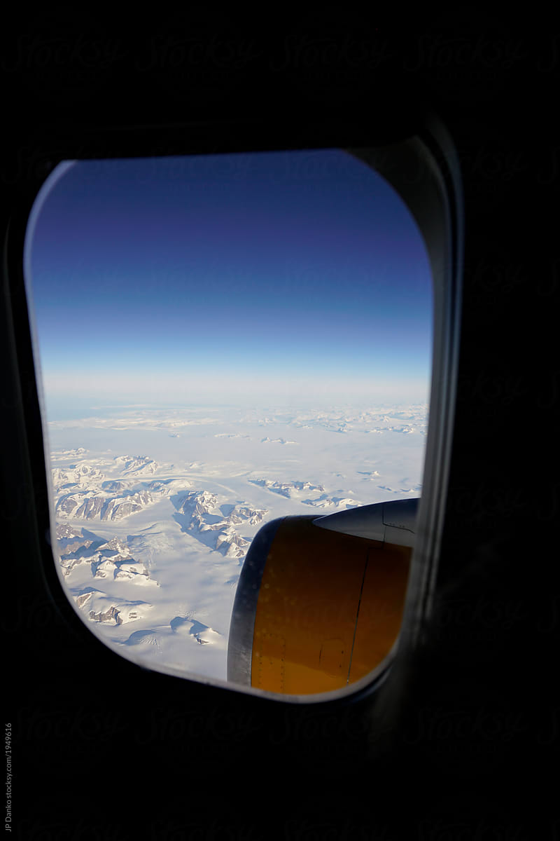 View of frozen landscape of Greenland through window of airplane