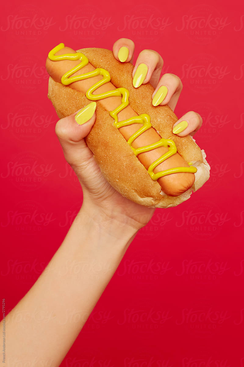 Woman\'s hand with yellow painted nails holds hotdog