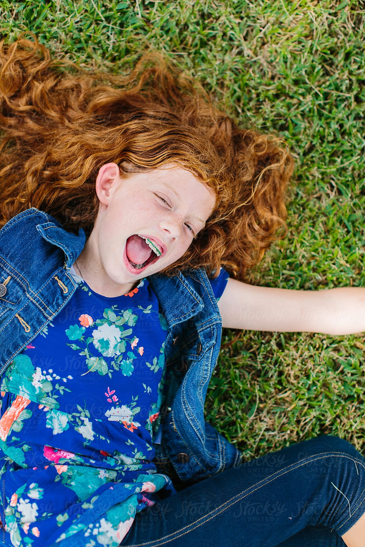 Smiling girl with beautiful brown red hair lying on the grass