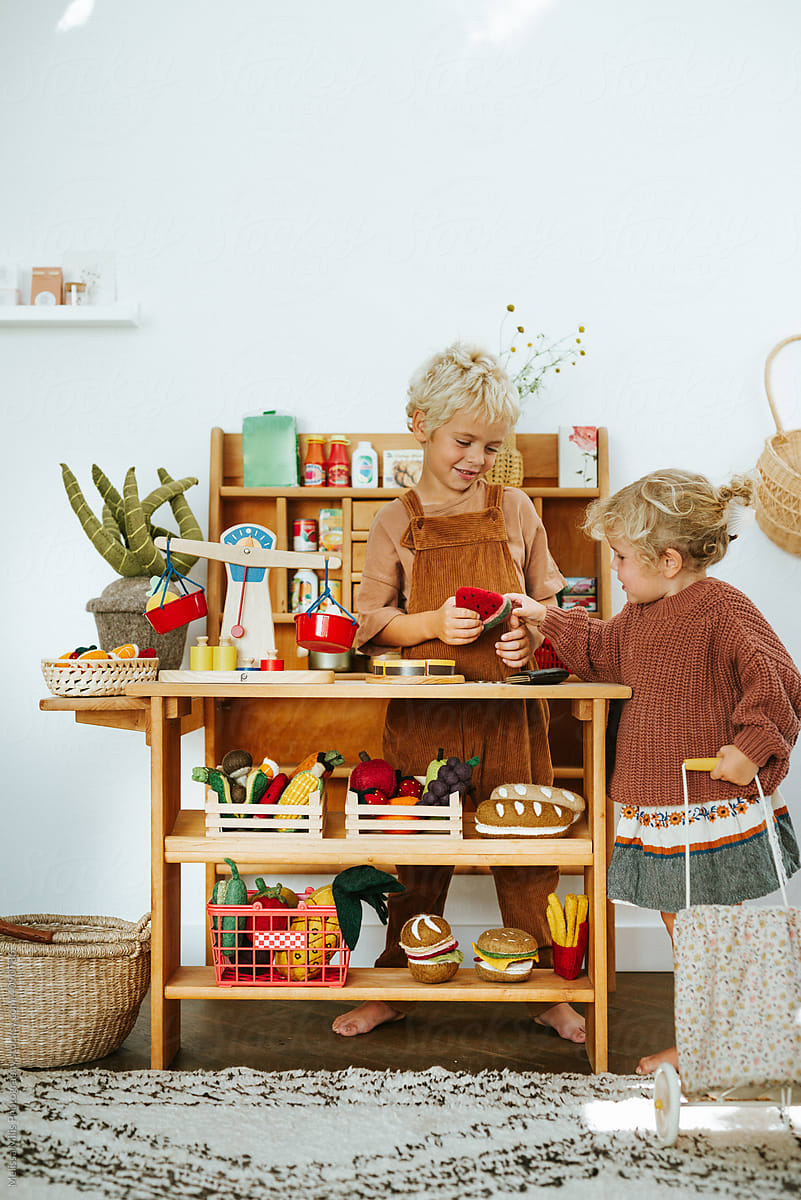 Siblings playing in a wooden play grocery store