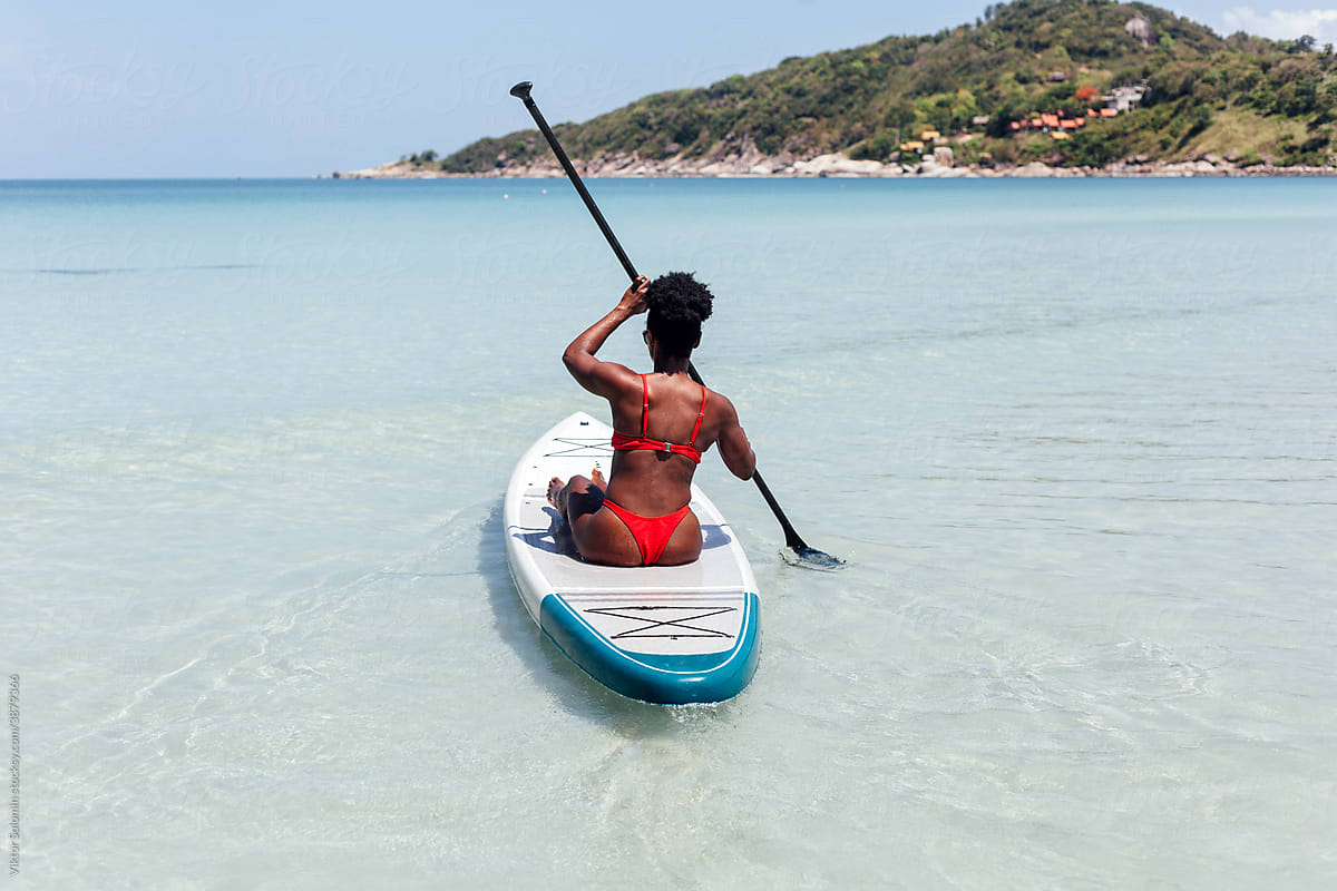 Unrecognizable black woman riding paddleboard in sea