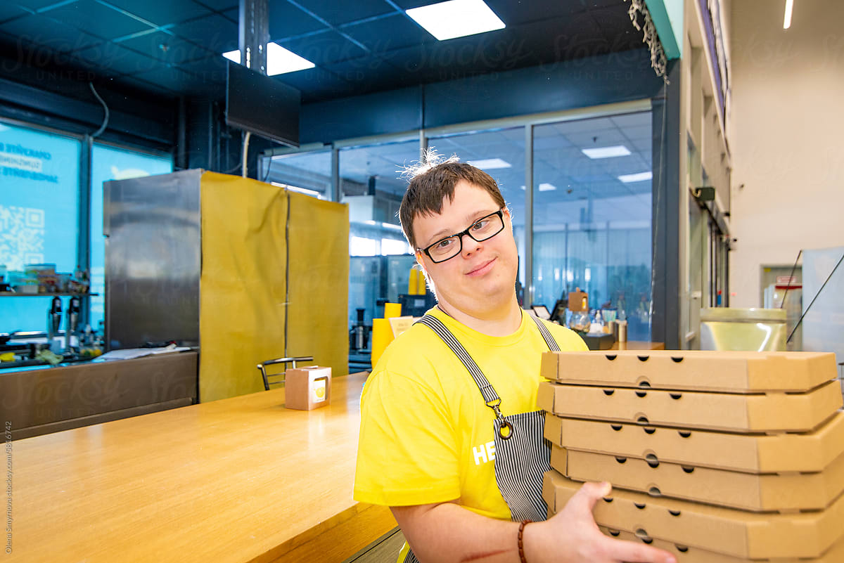 Young man with Down syndrome serves pizza in a pizzeria