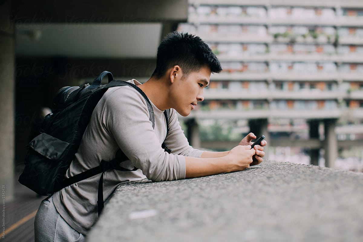 A Malaysian man leaning on a concrete ledge, using his mobile phone