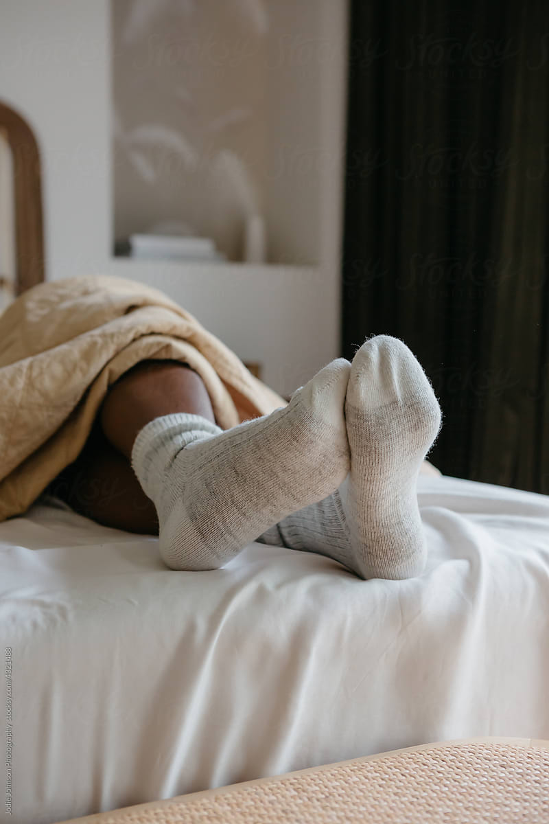 Feet with winter socks at the end of a bed