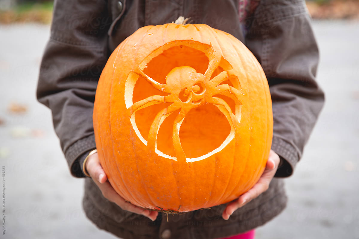 Child holding a pumpkin with a carved spider design