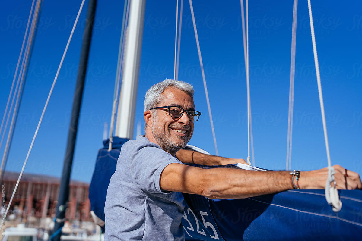 Positive senior man standing by yacht outdoors