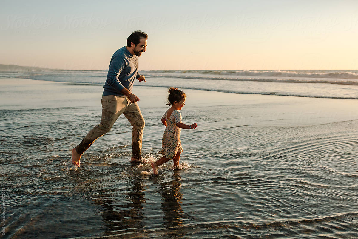 Father chasing daughter in ocean at sunset