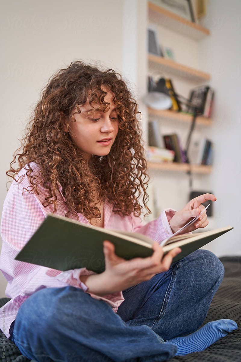 young curly woman reading a book at home