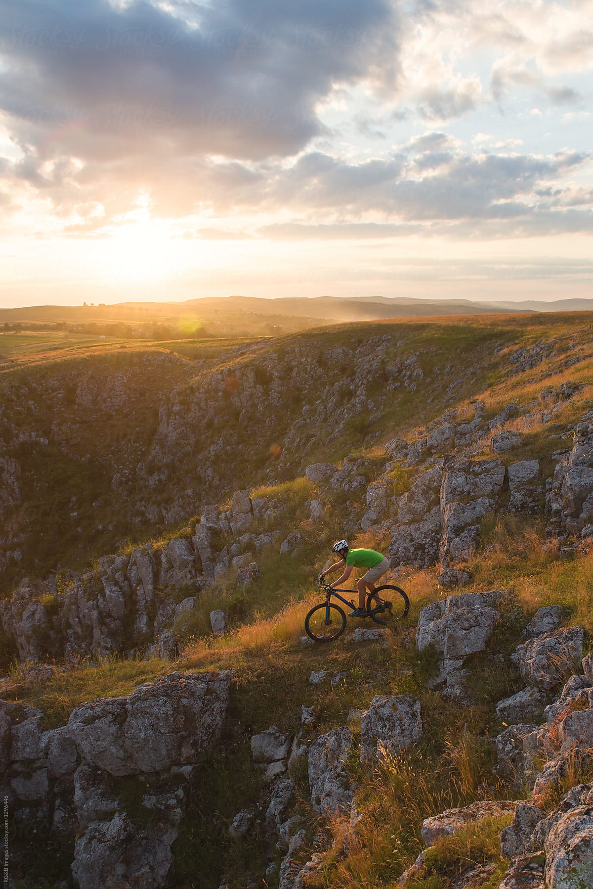 Man riding mountain bike downhill a craggy hill in the golden hour