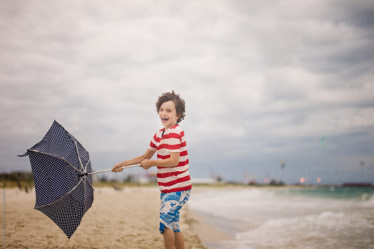 Boy smiling and struggling with an umbrella at the beach