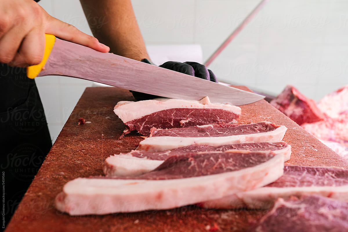 Crop butcher cutting raw meat on board in restaurant