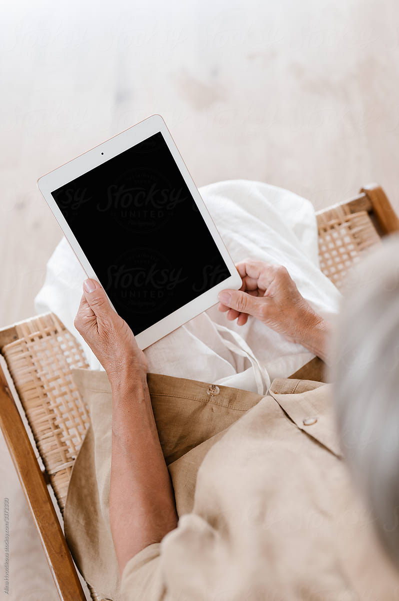 Crop senior woman using tablet on chair