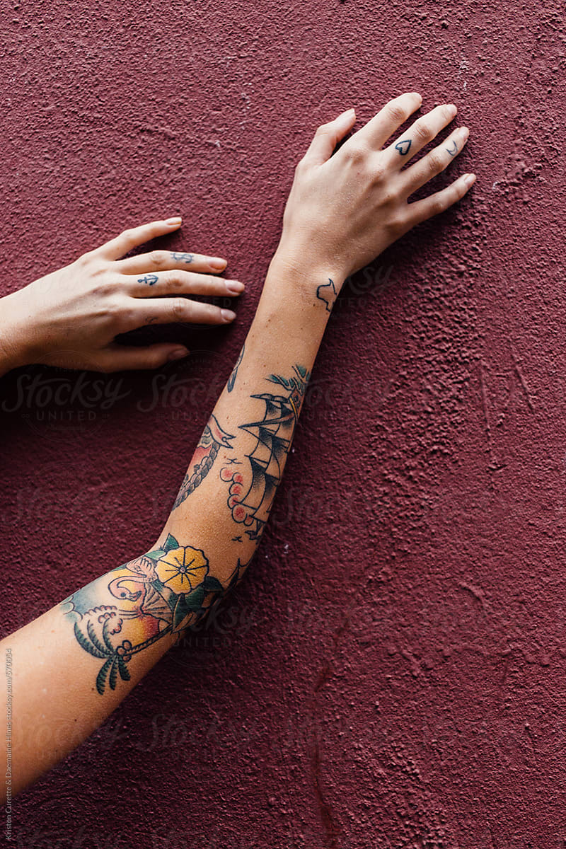 Tattooed arms reaching up a maroon concrete wall.