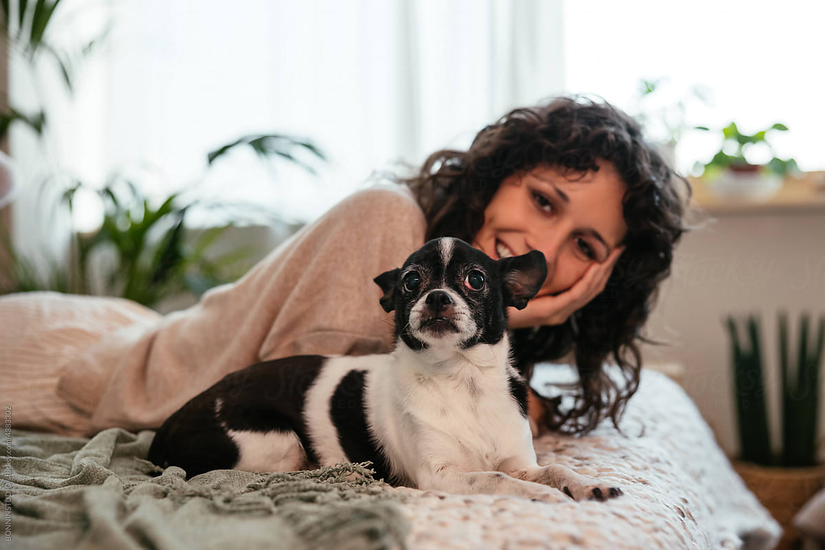 Smiling woman resting on bed with dog