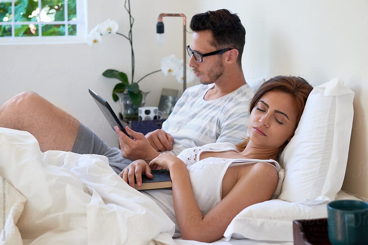 Beautiful woman sleeping while boyfriend reads on bed