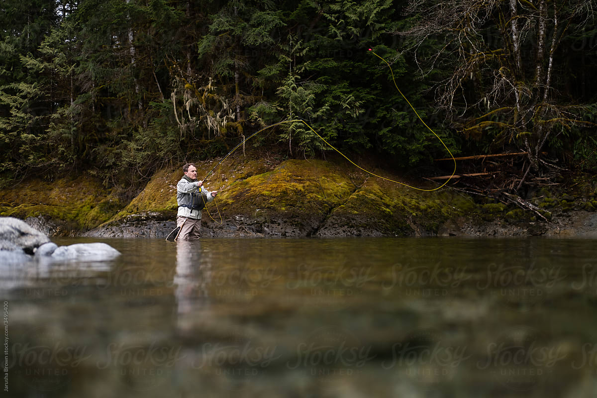 Fly fisherman wearing hip waders fishes in a stream.
