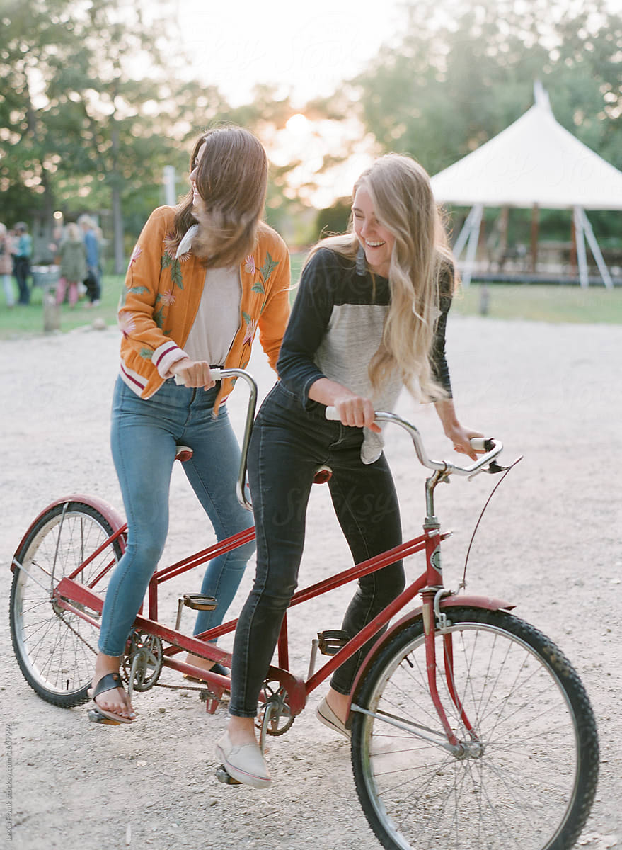 two millennial women ride a red tandem bike