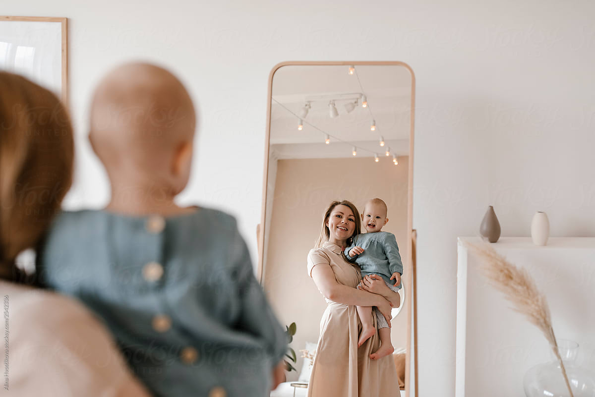 Mom holding kid by hands and showing reflection in mirror