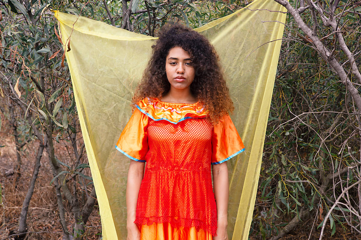 Girl with curly hair wearing orange dress in front of yellow backdrop
