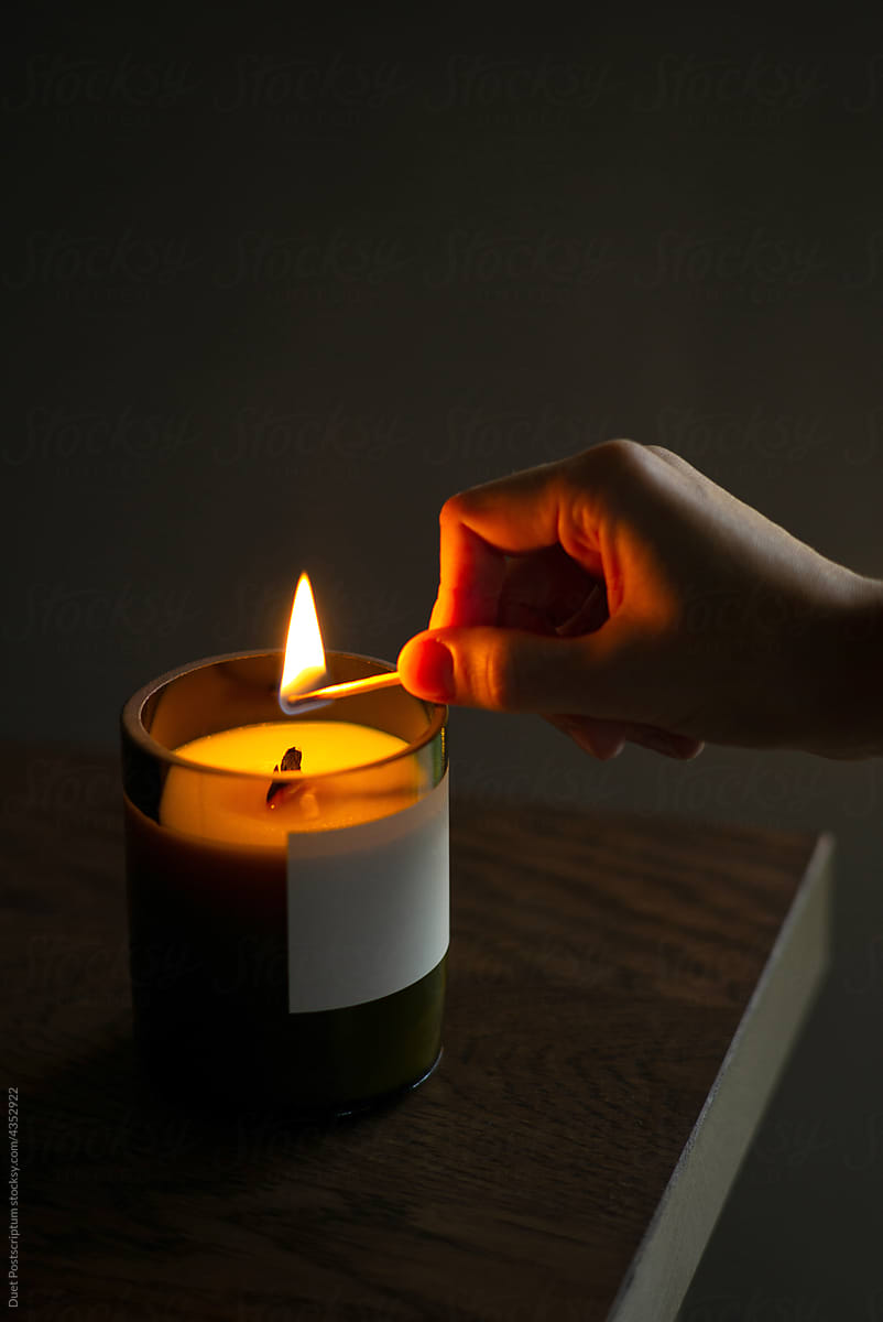 The hand of an unknown person brings a burning match to a scented candle