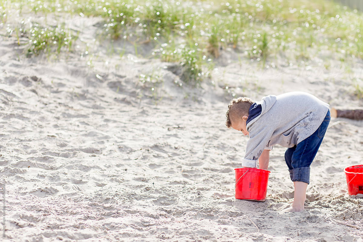 Boy digs in bucket on sandy beach