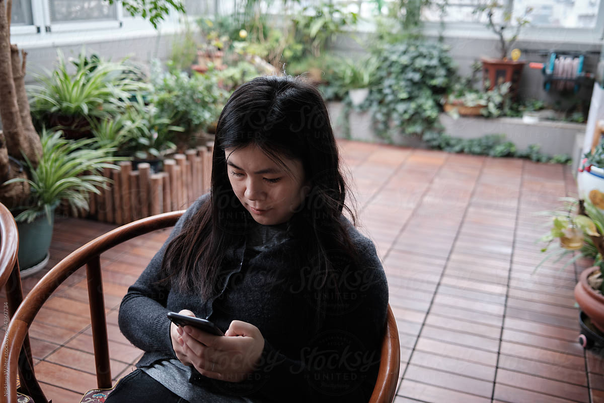 Chinese Woman Using Her Phone In An Indoor Garden.